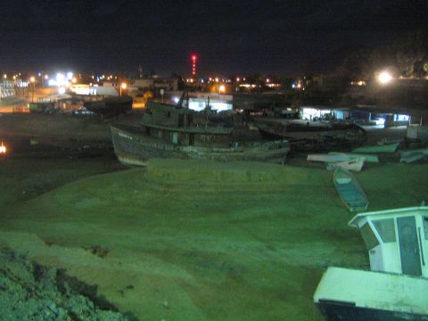 Cluster of beached boats on a dry harbor flat with town lights behind