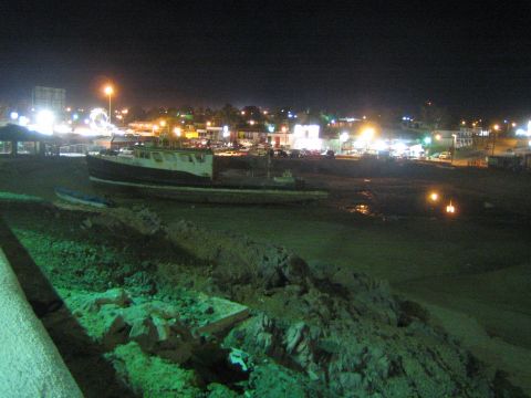 Beached boats on dry ground overlooking a brightly lit town at night