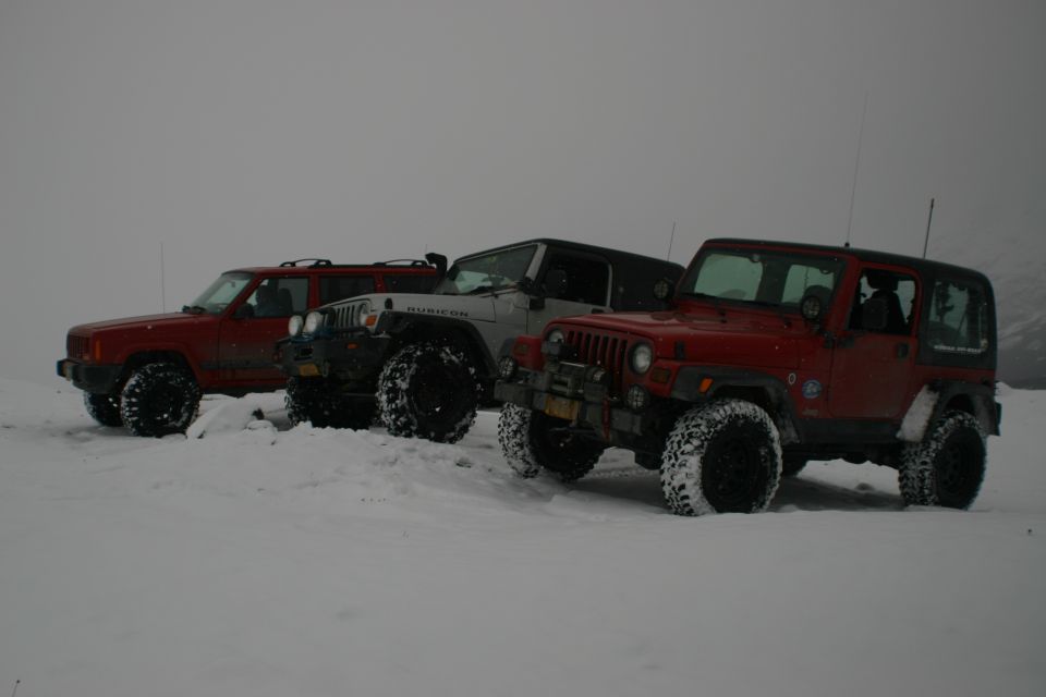 Three Jeeps and a Jeep Cherokee parked in the snow. The front Jeep is red, the middle is silver, and the rear is red. The Jeep Cherokee is red