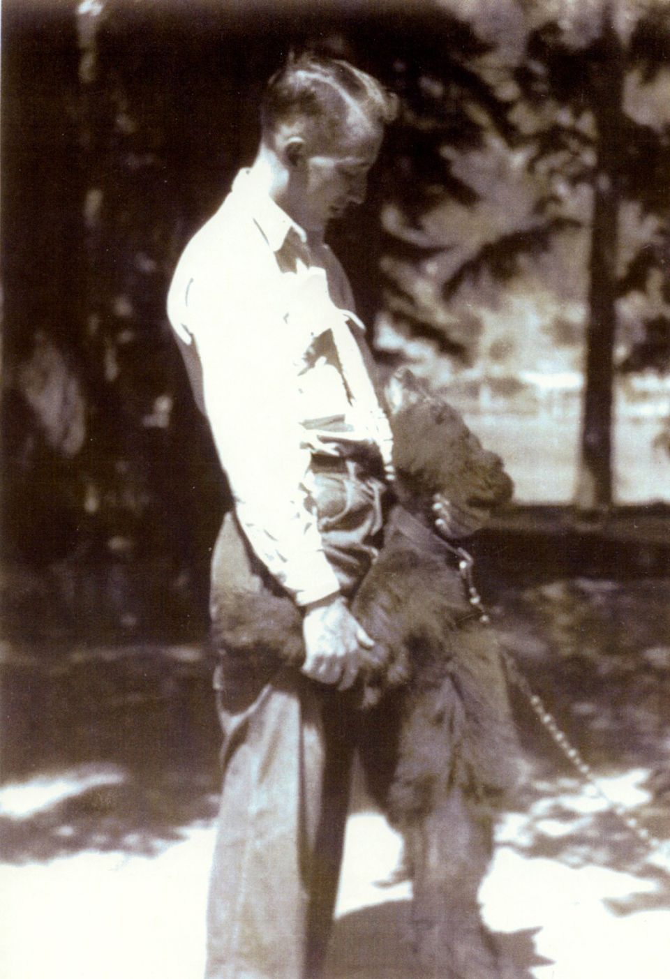Man holding a shaggy dog outdoors, with trees in the background