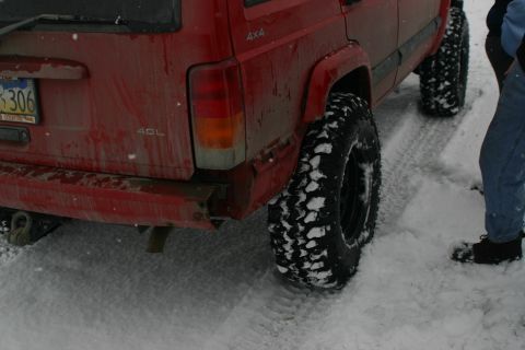 2003 Jeep TJ - Rear view of a red Jeep Cherokee XJ with large tires in the snow.