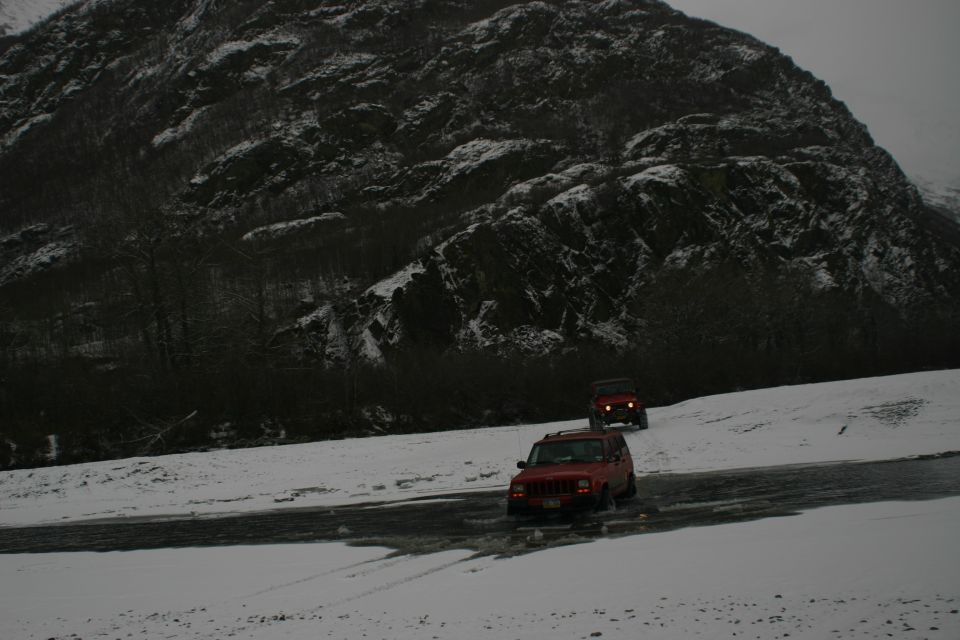 two red SUVs driving on a snowy road with a mountain in the background