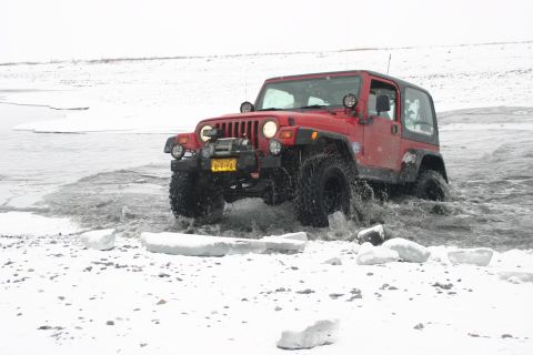 2003 Jeep TJ - A red 2003 Jeep TJ navigates through a snowy, icy landscape, splashing water as it drives.