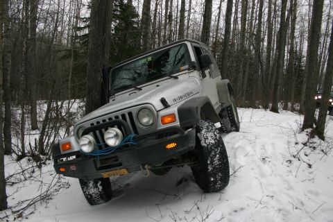 2003 Jeep TJ - A silver 2003 Jeep TJ Rubicon navigates a snowy trail through a forest.