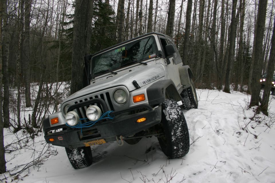 Silver 2003 Jeep TJ Rubicon in snow, front-left 3/4 view, with another vehicle visible in the background