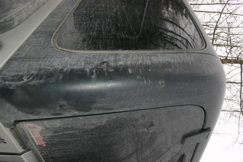 2003 Jeep TJ - Rear corner of a dark SUV with a camper shell, showing a dent and the 'Caribou' logo.