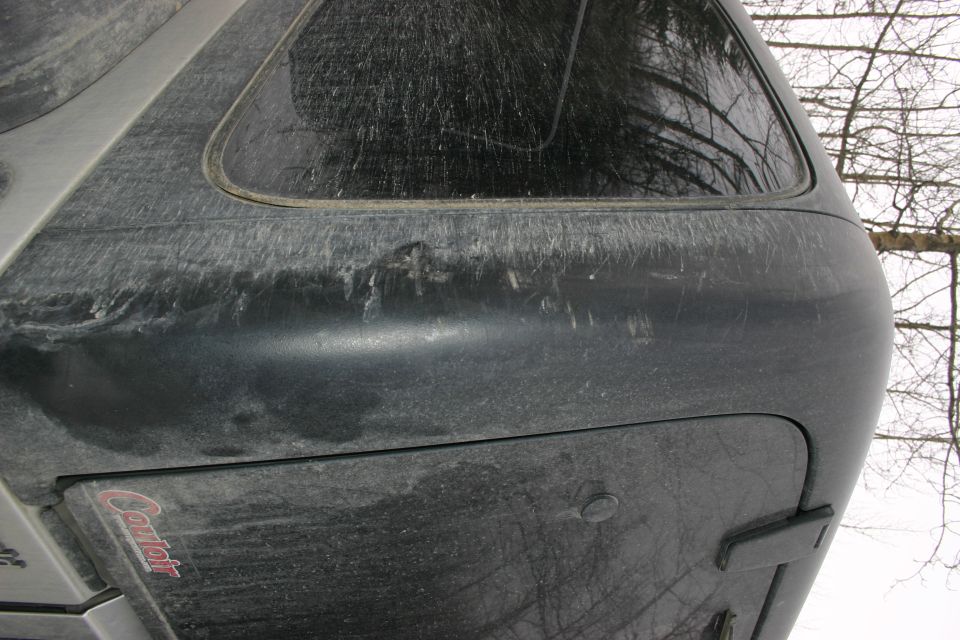 Rear corner of a dark SUV with a camper shell, showing a dent and the 'Caribou' logo on the shell