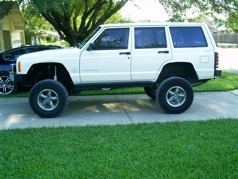 1986 Ford Bronco - A white Jeep Cherokee is parked on a concrete driveway next to a lawn.