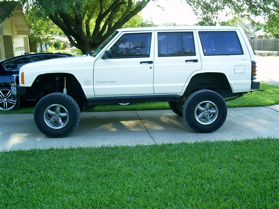 White Jeep Cherokee with lifted suspension and large tires parked on a driveway