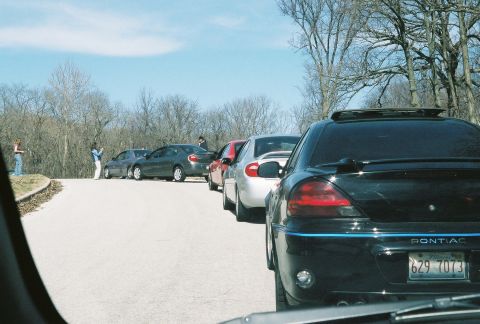 2004 Dodge SRT-4 - A group of cars are lined up on a paved road with bare trees and a bright sky overhead.
