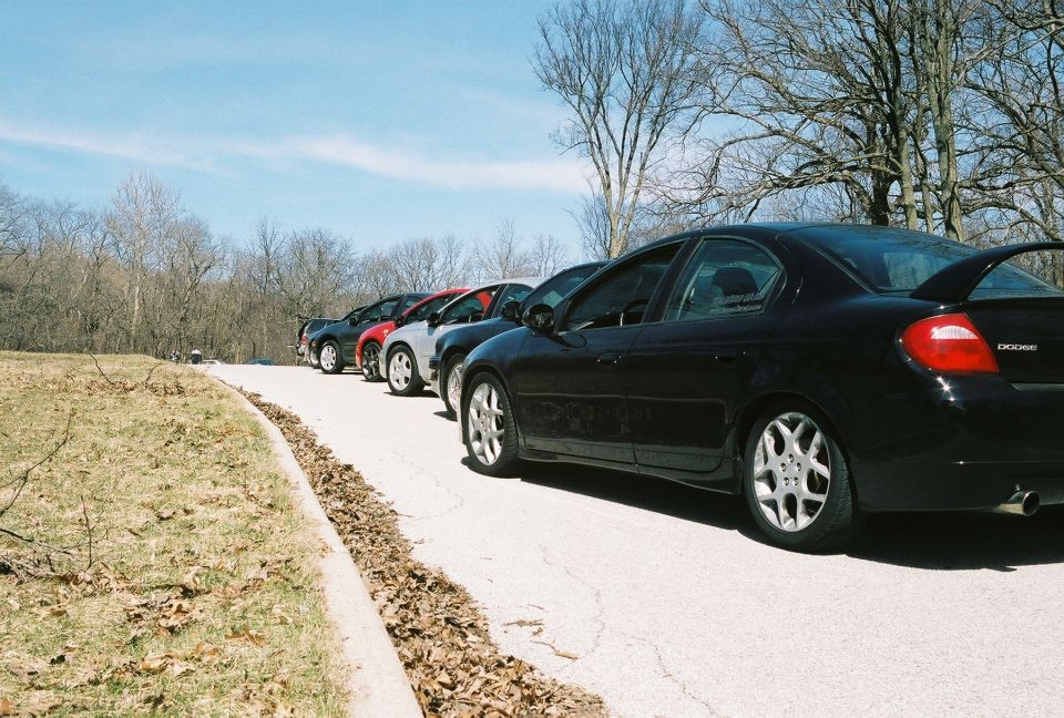 Black Dodge Neon SRT-4 with a rear spoiler, parked in a line of cars