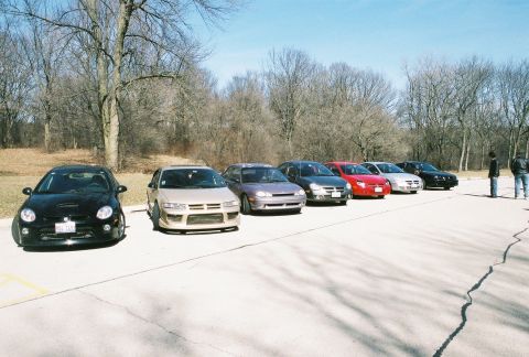 2004 Dodge SRT-4 - A group of cars are lined up in a parking lot on a clear day with bare trees.