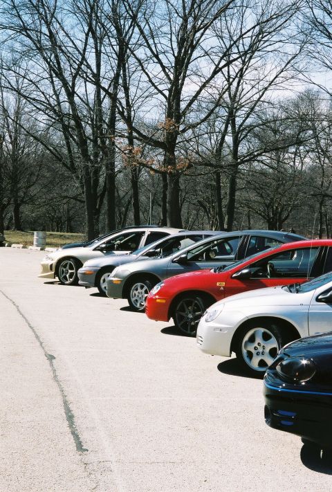 2004 Dodge SRT-4 - A line of cars, including two Dodge Neon SRT-4s, are parked in a lot with bare trees in the background.