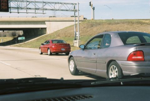 2004 Dodge SRT-4 - Two cars on the highway, a gray coupe in the foreground and a red sedan in the background.