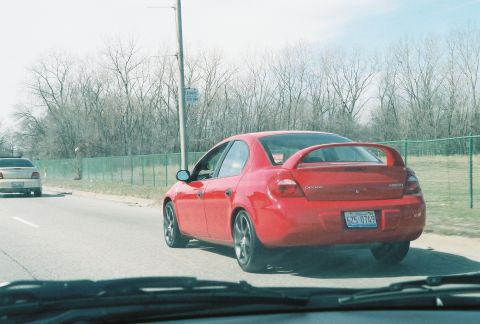2004 Dodge SRT-4 - A red 2004 Dodge SRT-4 is seen from the rear, driving on a road with another car ahead.