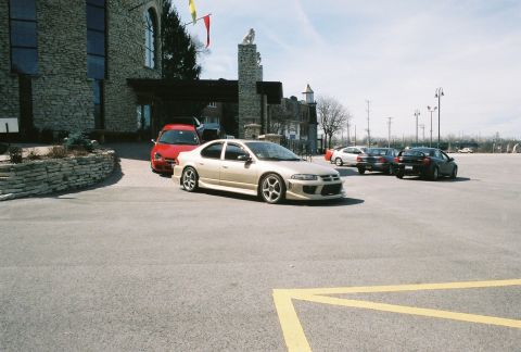 2004 Dodge SRT-4 - A gold sedan with custom body modifications is parked in a lot outside a stone building.