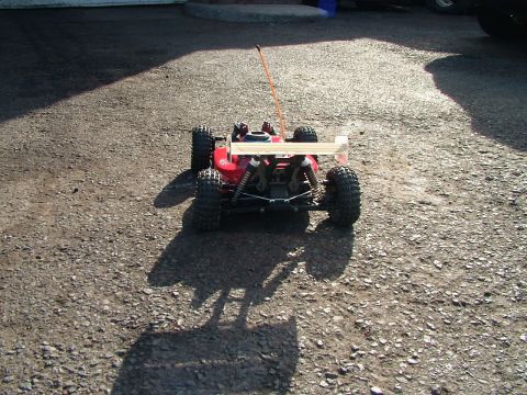 1994 Ford Bronco - A red remote control buggy with a prominent rear wing sits on a gravel surface, casting a long shadow.