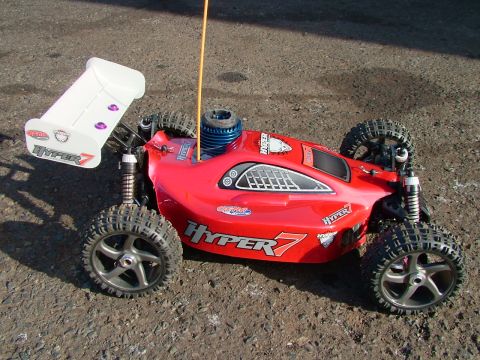 1994 Ford Bronco - A red remote control buggy with a prominent white spoiler sits on a gravelly surface.