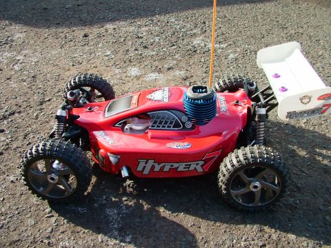 1994 Ford Bronco - A red remote control car with off-road tires and a prominent white spoiler is parked on a dirt surface.