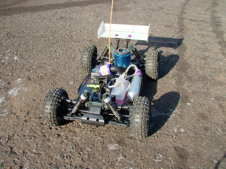 Radio-controlled nitro buggy with blue engine and white spoiler, parked on gravel