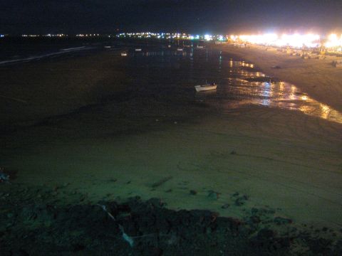 Dark beach at night with small boat and distant string of coastal lights