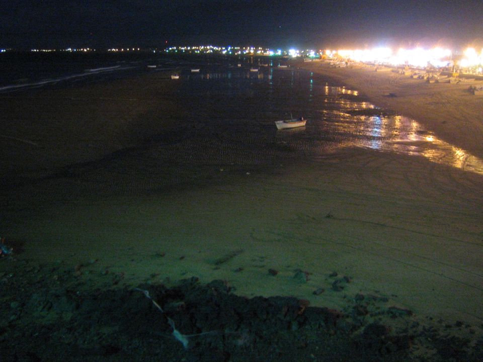 Dark beach at night with small boat and distant string of coastal lights
