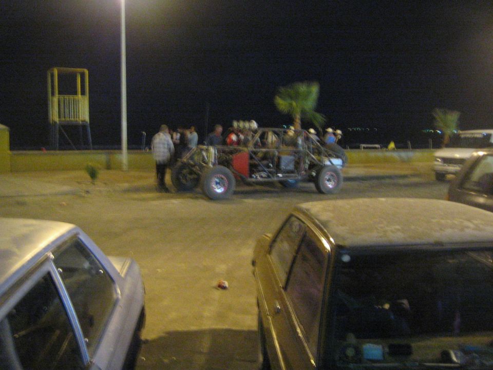 Tube-frame off-road buggy parked by lot with people and cars at night