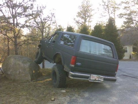 1995 Ford Mustang - A dark SUV is positioned with its front tire on a large rock, showing its rear profile.