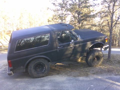 1995 Ford Mustang - This lifted black SUV is viewed from the side, parked on uneven terrain.