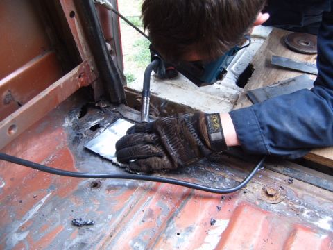 1988 Ford Bronco - A person is welding a patch onto a rusted floor pan inside a vehicle.