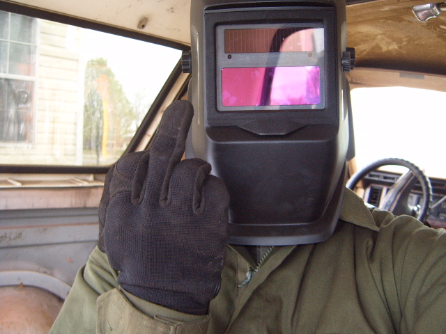 Person in welding mask inside a vehicle interior, giving the middle finger