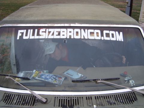 1988 Ford Bronco - A person is inside a vehicle, with a large sticker on the windshield and items on the dashboard.