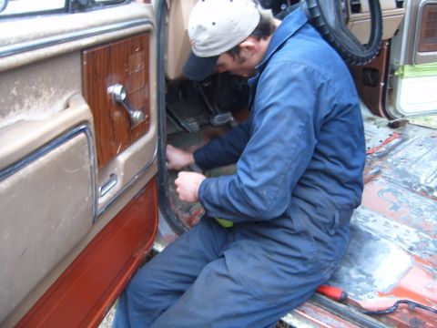 1988 Ford Bronco - A person works on the floor inside the cab of a vehicle, with a focus on the interior door panel.