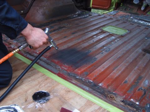 1988 Ford Bronco - The interior floor of a vehicle is being cleaned with a spray tool, revealing its ribbed metal construction.