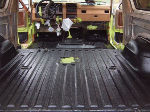 1988 Ford Bronco - The interior of a vintage SUV shows a black spray-lined cargo area and a tan dashboard with tape covering some sections.