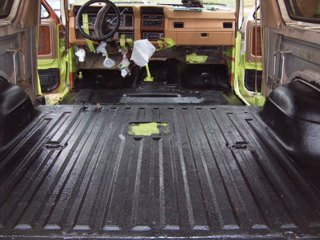 Interior of a vintage SUV with black spray-lined cargo area and tan dashboard. Tape covers parts of the interior