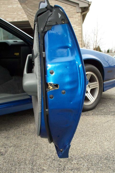 1990 Chevrolet Camaro - The open door of a blue Chevrolet Camaro reveals its interior and exterior details, with the front wheel and fender also in view.