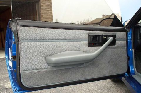 1990 Chevrolet Camaro - Close-up of a car's interior door panel, showing the handle and fabric upholstery.