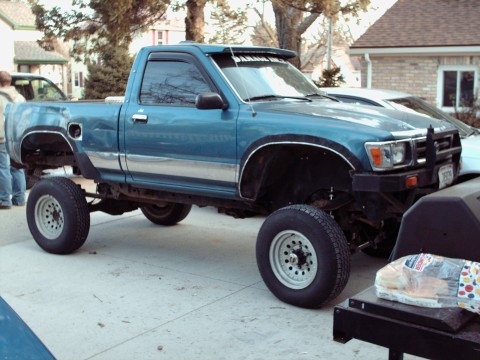 1977 Ford F-150 - A lifted blue pickup truck is parked in a driveway next to another vehicle.