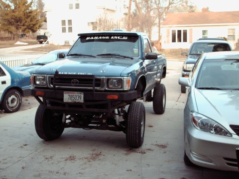 1977 Ford F-150 - A lifted blue pickup truck is parked in a driveway with other vehicles.
