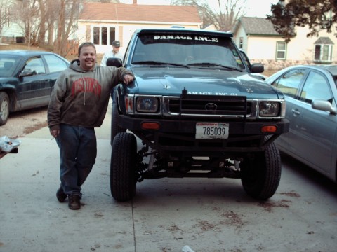 1977 Ford F-150 - A man poses with a lifted Toyota pickup truck, with other vehicles and houses in the background.