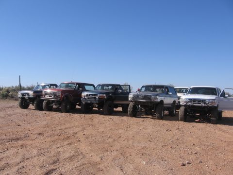 1990 Ford Bronco - A group of modified Ford trucks and Broncos are lined up in a desert landscape.