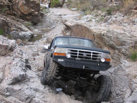 1990 Ford Bronco - Ford Bronco tackling a challenging off-road course in a rocky desert landscape.