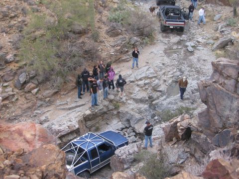1990 Ford Bronco - A group of people observe an off-road vehicle stuck in a rocky ravine during an excursion.