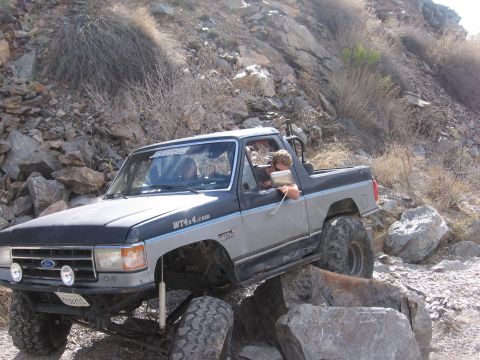 1990 Ford Bronco - This modified pickup truck is shown tackling a challenging off-road course with large rocks.