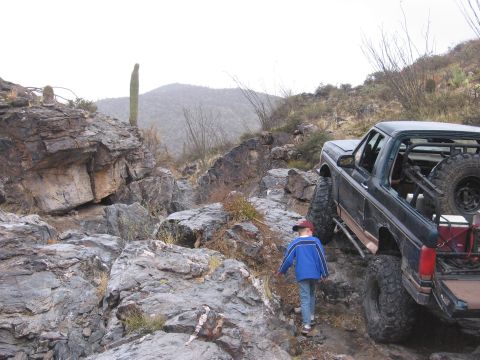 1990 Ford Bronco - A child walks near a modified Ford Bronco on a desert path with saguaro cacti in the background.
