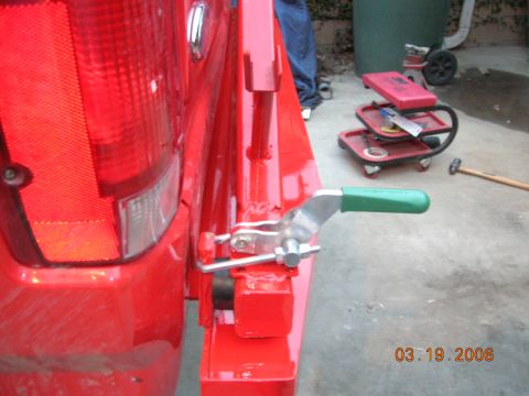1985 Ford Bronco - A close-up view of a red vehicle's rear bumper area, focusing on a tow hitch mechanism with a green handle.