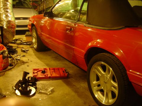 1986 Ford Mustang - A red 1986 Ford Mustang convertible is parked in a garage with tools scattered around, suggesting ongoing maintenance or a project.
