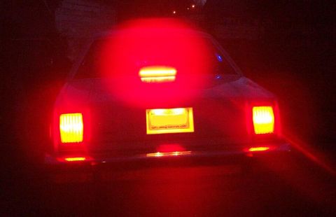 1985 Ford LTD Crown Victoria - Night rear view of a full-size sedan with the brakes applied, tail lights and a bar-style third brake light in the rear window glowing brig…