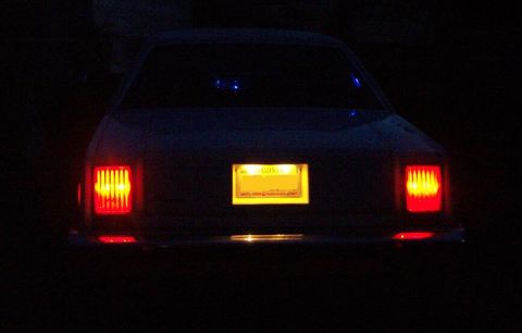 1985 Ford LTD Crown Victoria - Night shot of the rear of a full-size sedan with its tail lights lit, showing vertical-slat red lenses on either side of a yellow Virginia…